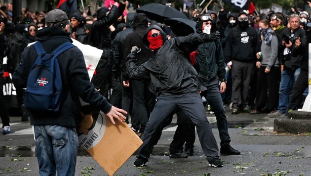 Vermummte Demonstranten werfen Steine gegen die Sicherheitskräfte. (Bild: AP)
