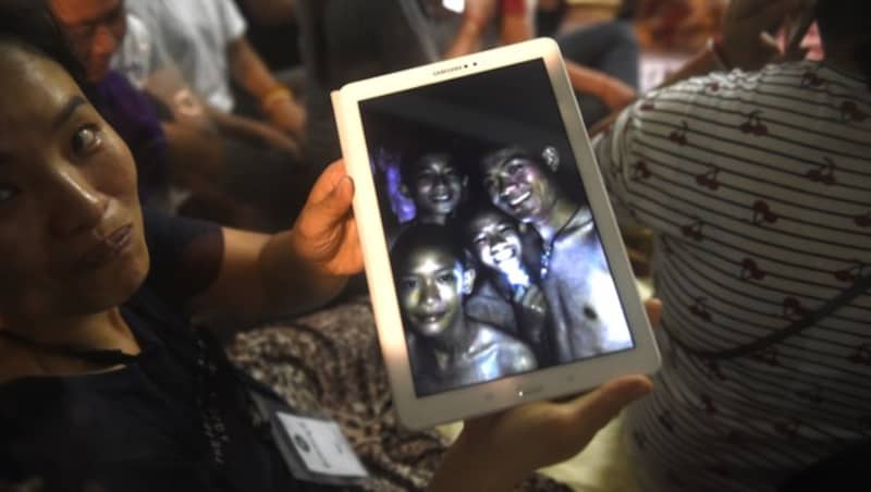 Glückliche Angehörige zeigen ein Bild aus der Höhle von den Kindern und ihrem Trainer. Das Foto wurde von Einsatzkräften aufgenommen. (Bild: AFP)