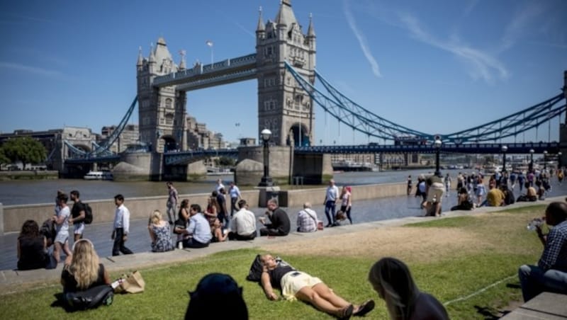 Eine Frau nimmt vor der traumhaften Kulisse der Tower Bridge ein Sonnenbad. (Bild: AFP or licensors)