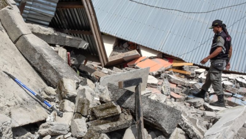 Ein Helfer klettert über die eingestürzten Ruinen eines Hauses nach dem Erdbeben in Lombok. (Bild: AFP )