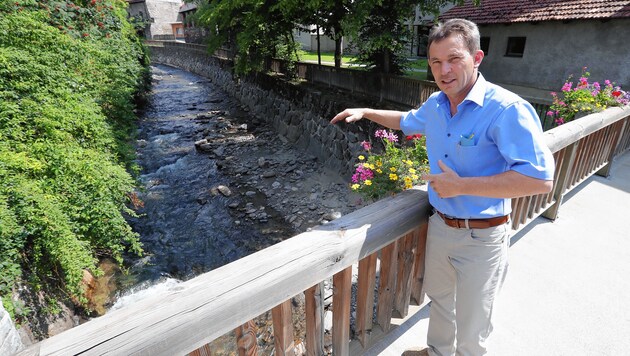 Bürgermeister Johann Schmidhofer (VP) zeigt, wie hoch das Wasser dieses Bachs vor einem Jahr stand. (Bild: Juergen Radspieler)