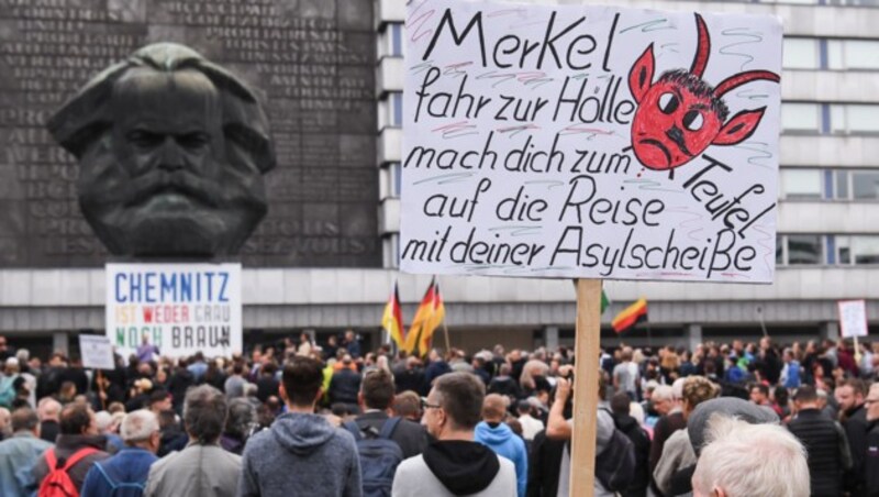 Ein Teilnehmer bei der Kundgebung von Pro Chemnitz hält vor dem Karl-Marx-Denkmal ein Schild mit der Aufschrift „Merkel fahr zur Hölle, mach dich zum Teufel, auf die Reise mit deiner Asylscheiße“. (Bild: APA/dpa/Ralf Hirschberger)