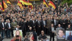 Demonstranten halten bei einer AfD-Veranstaltung Schilder mit Bildern hoch, die angeblich von Migranten getötete Bürger zeigen sollen. (Bild: AP)