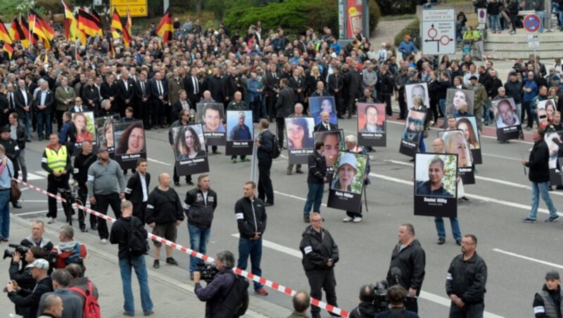 Demonstranten halten bei der AfD-Veranstaltung Schilder mit Bildern hoch, die von Migranten getötete Bürger zeigen sollen. (Bild: AP)