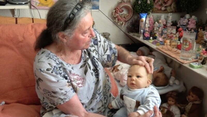 Barbara Mosler mit einer ihrer Reborn-Puppen. Im Hintergrund ist ihre beeindruckende Puppensammlung zu erkennen. (Bild: krone.at)