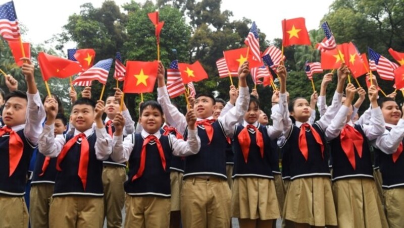 Kinder halten US- und Vietnam-Fahnen vor der Ankunft Trumps in Hanoi in die Höhe. (Bild: AFP)