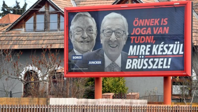 März 2019: Ein Fidesz-Plakat mit dem ungarischstämmigen US-Investor George Soros und dem damaligen EU-Kommissionspräsident Juncker, das nahelegt, diese würden gezielt Migrationsströme Richtung Europa steuern (Bild: APA/AFP/Attila Kisbenedek)