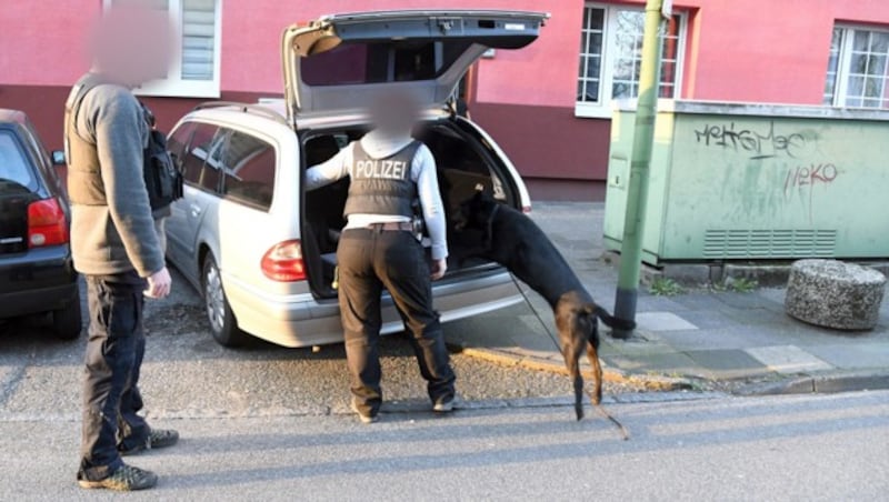 Polizisten mit einem Spürhund durchsuchen ein Auto im Rahmen eines Großeinsatzes gegen mutmaßliche IS-Anhänger in Essen. (Bild: APA/Stephan Witte)