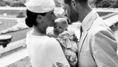 Harry und Meghan wenden sich im Garten von Schloss Windsor einander liebevoll zu. Meghan hält den in seinem voluminösen Taufkleid selig schlummernden Archie im Arm. (Bild: AFP)