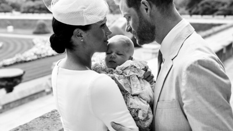 Harry und Meghan wenden sich im Garten von Schloss Windsor einander liebevoll zu. Meghan hält den in seinem voluminösen Taufkleid selig schlummernden Archie im Arm. (Bild: AFP)