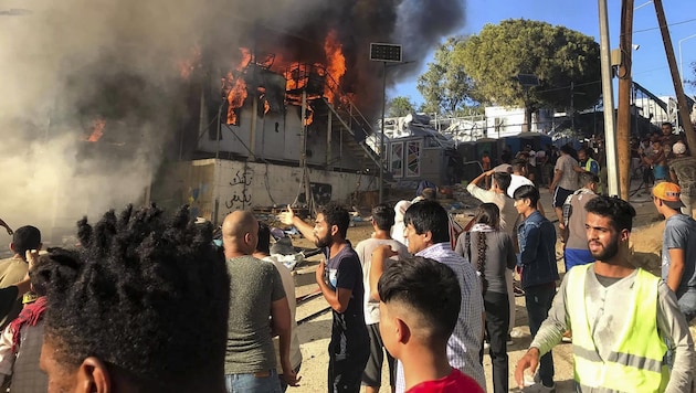 Lesbos: Flüchtlinge stehen neben brennenden Hauscontainern (Bild: AP)