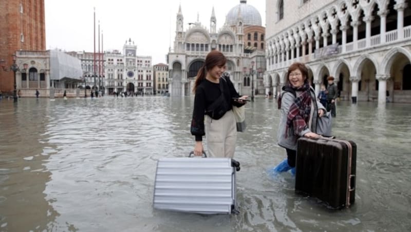 Diesen Touristinnen kann das Hochwasser am Freitag nicht die gute Laune verderben. (Bild: AP)