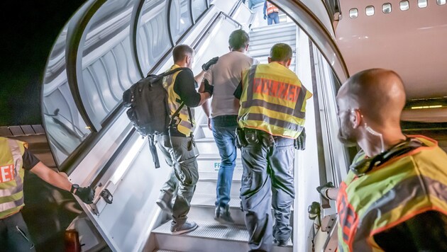 Polizeibeamte begleiten einen Afghanen auf dem Flughafen Leipzig-Halle in ein Charterflugzeug. (Archivbild) (Bild: APA/dpa/Michael Kappeler)