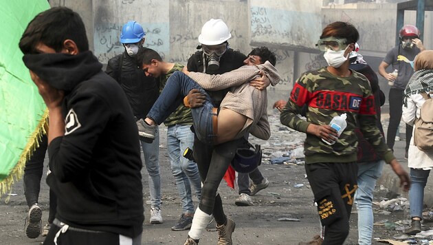 Ein Regierungsgegner bringt bei Auseinandersetzungen mit den Sicherheitskräften in Bagdad einen verletzten Kollegen in Sicherheit. (Bild: AP)