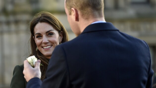 Prinz William hält der lächelnden Herzogin Kate eine weiße Rose hin. (Bild: APA/AP)