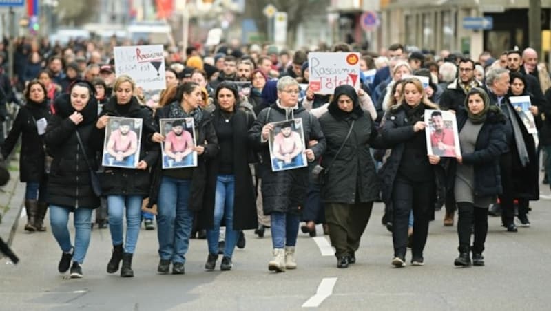 Zahlreiche Menschen gehen bei einem Trauermarsch vom Tatort Heumarkt zum Tatort Kurt-Schumacher-Platz und halten dabei Fotos der Opfer in den Händen. (Bild: APA/dpa/Nicolas Armer)