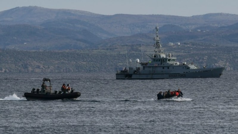 Migranten auf dem Weg nach Lesbos, im Hintergrund die HMC Valiant, die im Auftrag von Frontex patrouilliert (Bild: AFP)