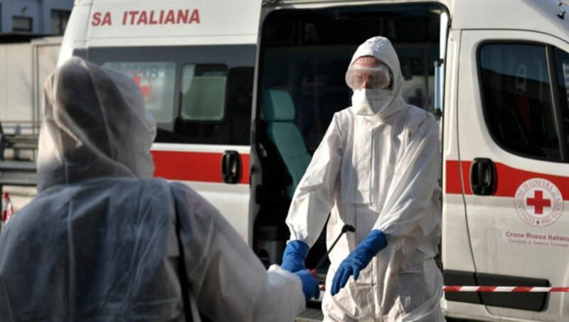 Rettungssanitäter in Italien helfen sich gegenseitig beim Desinfizieren nach einem Einsatz. (Bild: AP)