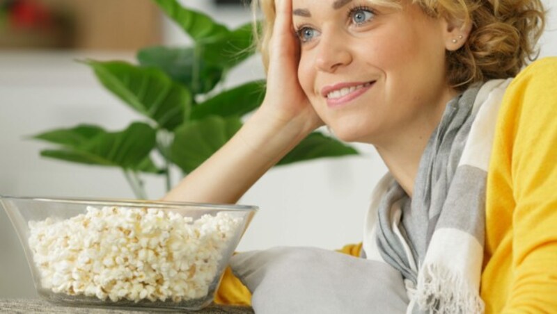 woman laying on the sofa holding bowl popcorn (Bild: ©auremar - stock.adobe.com)