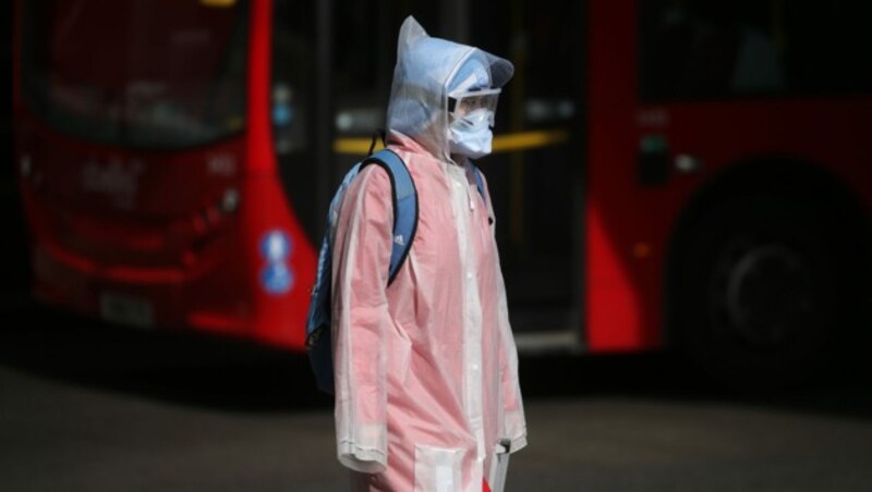 Sicher ist sicher - dieser britische Passant trägt in London Schutzmaske, Schutzbrille und noch dazu eine Jacke mit Kapuze sowie Schirm. (Bild: AFP)