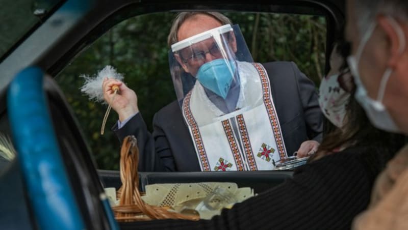 Dieser ukrainische Priester weiht die Osterkörbe im Auto von Gläubigen - gut geschützt mit Visier. (Bild: AFP )