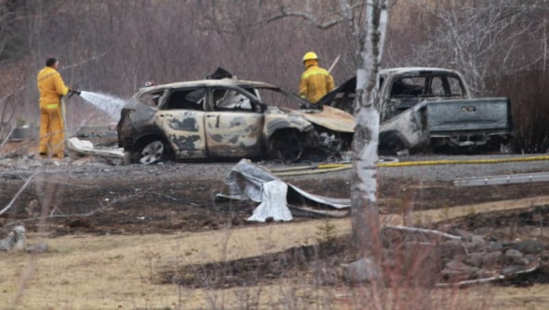 Feuerwehrmänner löschen Autos, die von dem Amokläufer in Brand gesteckt wurden. (Bild: AP)