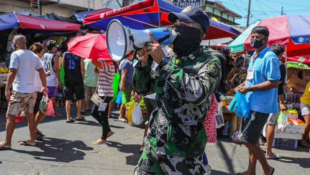 Ein philippinischer Soldat macht die einkaufenden Menschen darauf aufmerksam, dass sie die Regeln des Social Distancing befolgen sollen. (Bild: AFP)