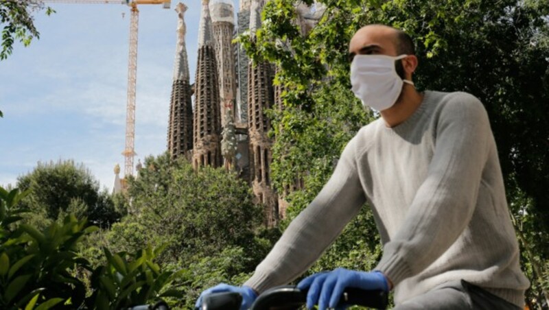 Dieser Radfahrer vor der Sagrada Familia in Barcelona geht mit Mundschutz und Handschuhen auf Nummer sicher. (Bild: AFP)