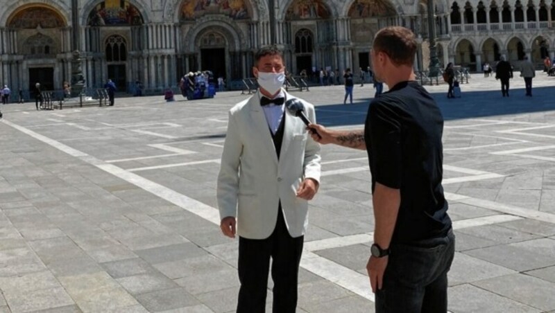 „Krone“-Interview mit Traditionskellner Riccardo mitten auf dem Markusplatz. Der Blick auf „seinen“ Gastgarten stimmt den Italiener traurig. (Bild: Klaus Loibnegger)