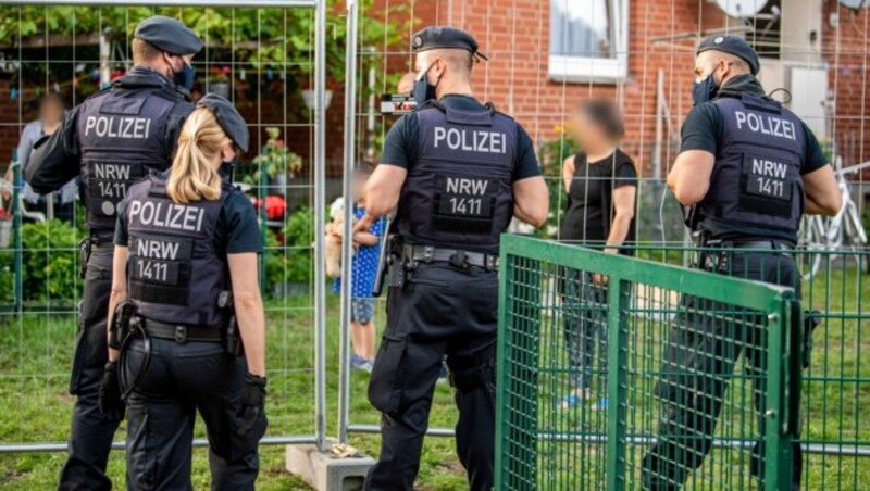 Polizisten sprechen mit Bewohnern, die hinter einem Bauzaun unter Quarantäne stehen. Die Stadt Verl hat nach positiven Corona-Tests bei zahlreichen Tönnies-Mitarbeitern Quarantäne eingerichtet. (Bild: APA/dpa/David Inderlied)