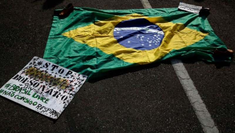 Eine brasilianische Flagge mit eine Transparent mit den portugiesischen Worten „Stoppt Bolsonaro, Freiheit für Brasilien, Ich kann nicht atmen“ liegt am Boden. (Bild: AP)