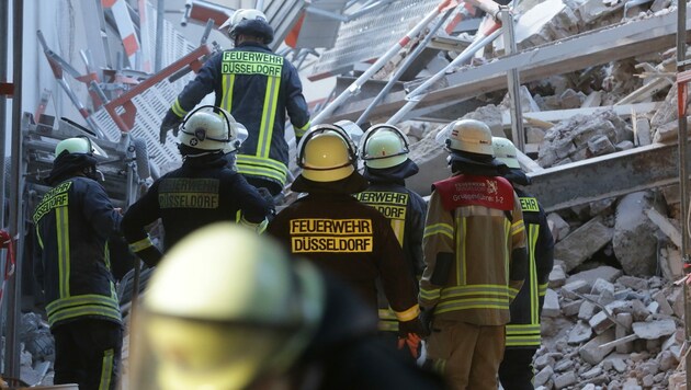Feuerwehrleute stehen in einer Hauseinfahrt vor Bauschutt. Im Düsseldorfer Zentrum waren bei Bauarbeiten am Montag Teile eines Gebäudes eingestürzt. (Bild: APA/dpa/David Young)