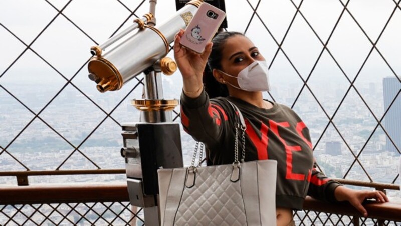 Eine Touristin macht ein Selfie am Eiffelturm in Paris - vorbildlich mit Maske. (Bild: AFP)