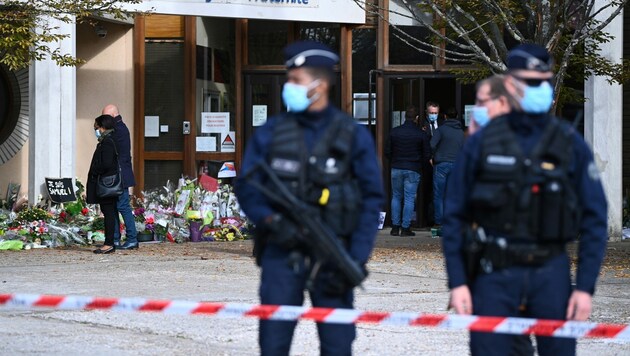 Immer mehr Blumen, Transparente und Kerzen werden für den getöteten Lehrer vor seiner Schule abgelegt. (Bild: APA/AFP/Anne-Christine POUJOULAT)