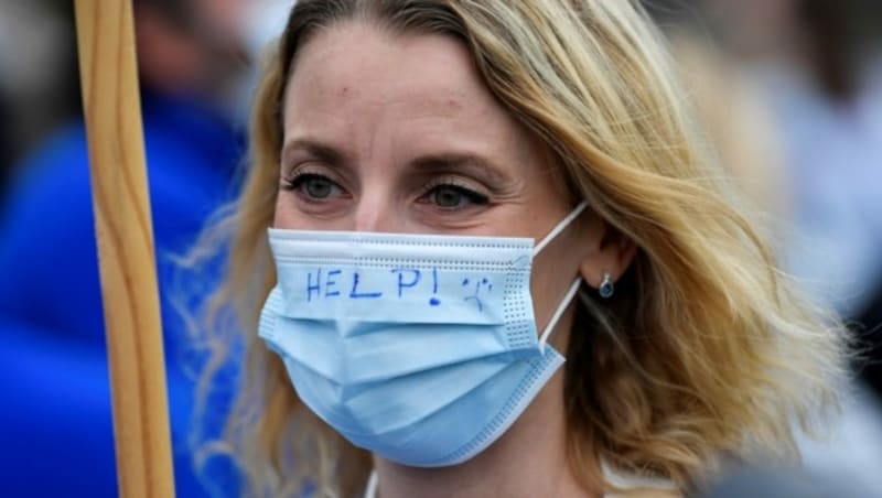 Diese Frau scheint mit ihrer Maske um Hilfe rufen zu wollen. (Bild: JOHN THYS/AFP (Symbolbild))