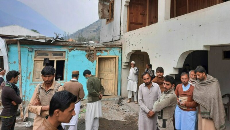 Menschen vor einem von Artilleriefeuer teilweise zerstörten Haus im pakistanischen Teil der Kaschmir-Region. (Bild: AP)