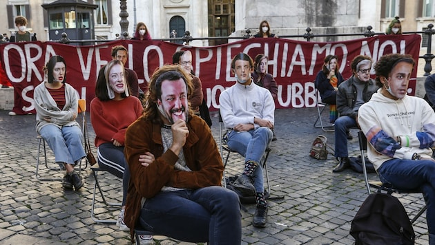 Studenten protestieren sitzend in Rom - sie tragen dabei Gesichter von Politikern als Maske. (Bild: LaPresse)