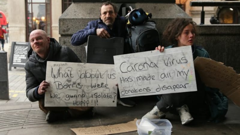 Obdachlose halten Schilder hoch mit der Aufschrift „Was ist mit uns, Hilfe!“, und „Das Corona-Virus hat alle meine Spenden verschwinden lassen“ (Bild: APA/AFP/ISABEL INFANTES)