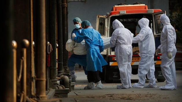 Verwandte und medizinisches Personal tragen den Körper eines Covid-19-Opfers ins Krematorium. (Bild: ASSOCIATED PRESS)