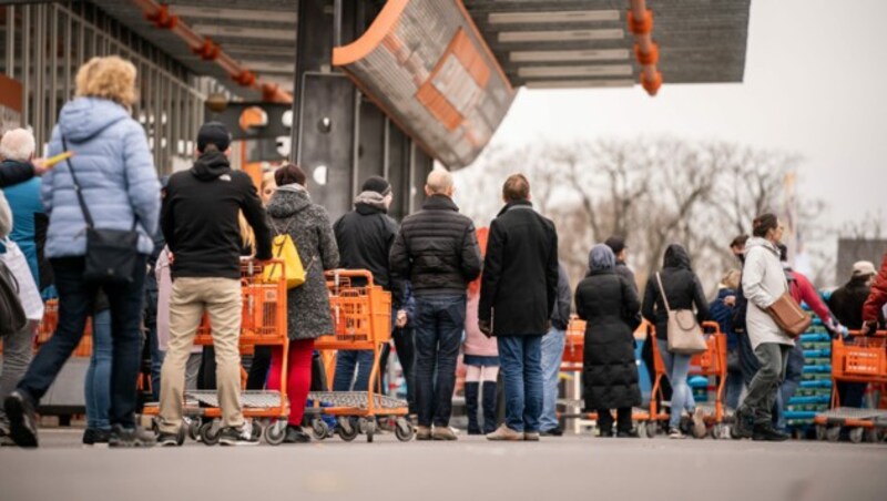 Einkäufer stehen in einer Schlange vor einem Baumarkt. Sie werden durch das Sicherheitspersonal nur einzeln eingelassen. (Bild: APA/dpa/Michael Kappeler)