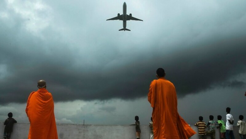 Mönche und Schüler beobachten ein aus Kalkutta startendes Flugzeug. (Bild: APA/AFP/Dibyangshu SARKAR)