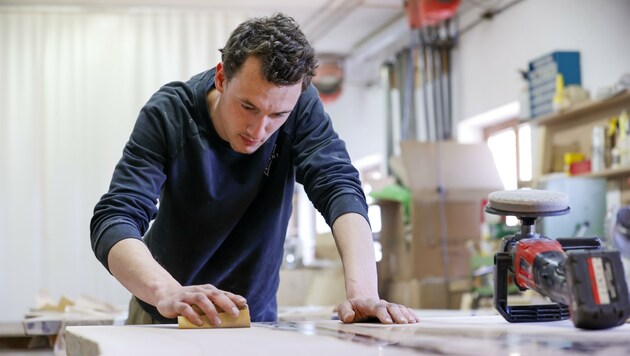 Rupert Wallmann schleift eine der Eschen-Holzplatten. Jede Tischplatte muss zumindest achtmal geschliffen werden. (Bild: Tschepp Markus)