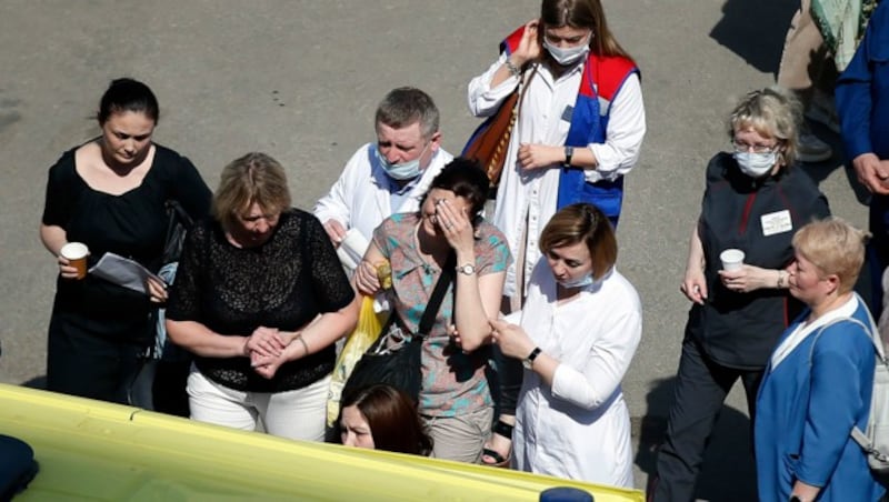 Rettungskräfte helfen trauernden Eltern vor dem abgesperrten Schulgelände. (Bild: AP)