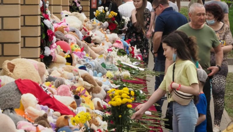 Menschen legen vor der Schule Blumen und Stofftiere nieder. (Bild: AP Photo/Dmitri Lovetsky)