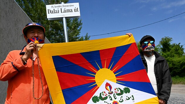 Aktivisten mit der tibetischen Flagge vor dem Schild der Dalai-Lama-Straße in Budapest (Bild: APA/AFP/Attila KISBENEDEK)
