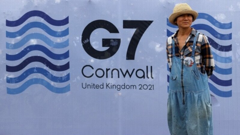 Ein Fußgänger posiert vor einem Plakat des G7-Gipfels in Cornwall, Großbritannien. (Bild: AFP)