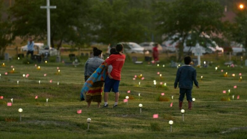 Eine Familie spaziert durch ein Feld, wo Fahnen und Solarleuchten den Ort markieren, an dem menschliche Überreste in unmarkierten Gräbern auf dem Gelände der ehemaligen Marieval Indian Residential School entdeckt wurden. (Bild: Geoff Robins / AFP)