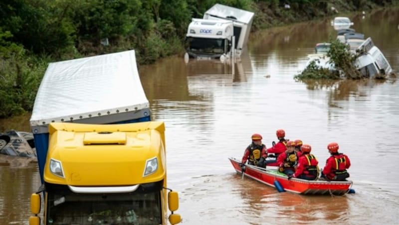 Helfer der Wasserwacht untersuchen von einem Boot aus Lastwagen, die auf der überfluteten Bundesstraße 265 stehen. (Bild: APA/dpa/Marius Becker)