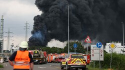 Leverkusen: Einsatzfahrzeuge der Feuerwehr stehen unweit einer Zufahrt zum Chemiepark über dem eine dunkle Rauchwolke aufsteigt. (Bild: APA/dpa/Oliver Berg)