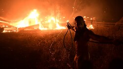 Es sind diese Bilder der Machtlosigkeit, die Griechenland verzweifeln lassen: Mit dem Mut der Verzweiflung steht ein Mann vor den meterhohen Flammen und versucht, mit einem Gartenschlauch das Feuer zu löschen. (Bild: The Associated Press)